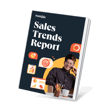 Sales Trends Report booklet with a smiling young man wearing glasses, talking on a phone while sitting at a desk adorned with pens and a coffee cup, against a dark background featuring colorful graphic elements.